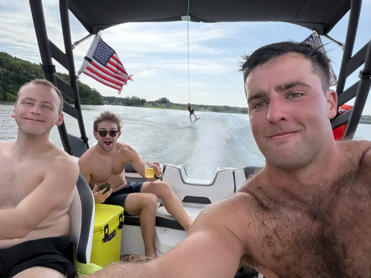 Three friends on a wake boat with a wakeboarder behind them